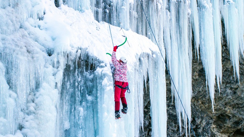 Ice climber scaling frozen waterfall, highlighting Austria's diverse winter activities.