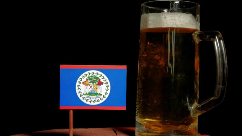 Frosty mug of Belikin beer next to Belize flag, symbolizing local pride.