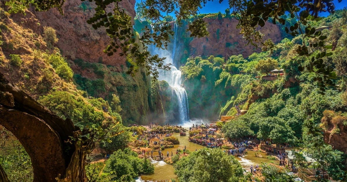 Crowded viewing area at the base of Ouzoud Waterfalls on a sunny day.