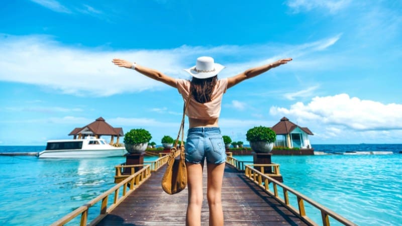 Woman on a dock, arms outstretched, deciding which Maldives island to choose.